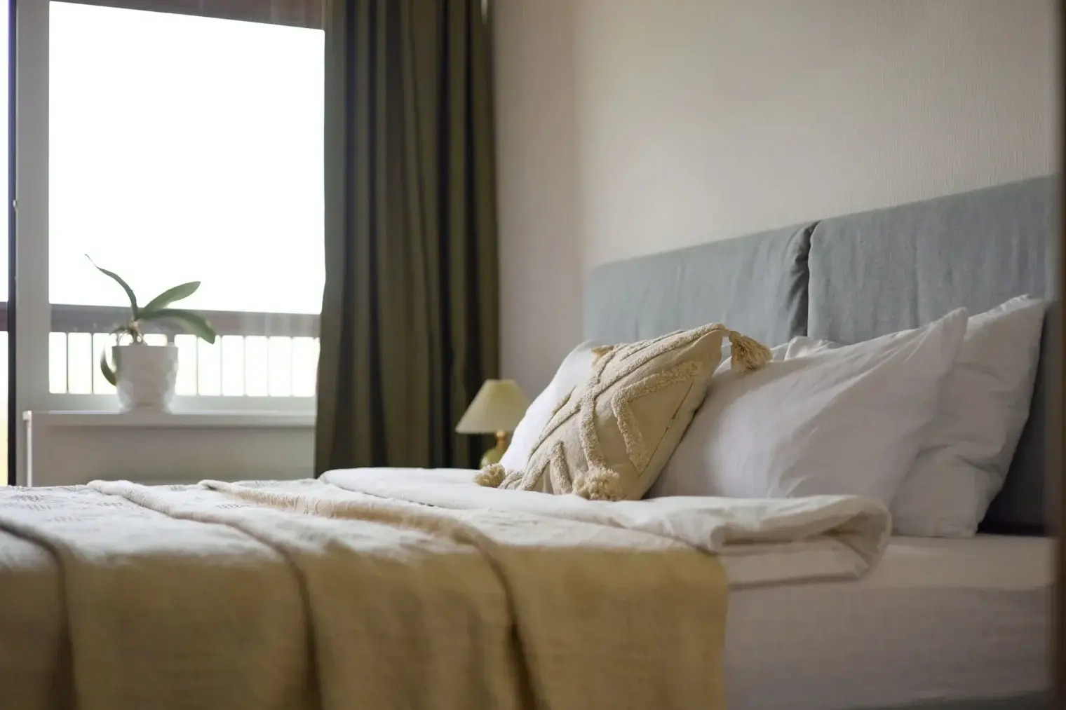 Plush bed holding layered pillows and catching soft window light inside an Ivory on Long Creek apartment bedroom.