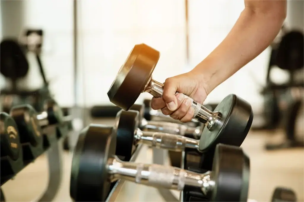Resident gripping a chrome dumbbell rising from the weight rack inside the Ivory on Long Creek fitness center.
