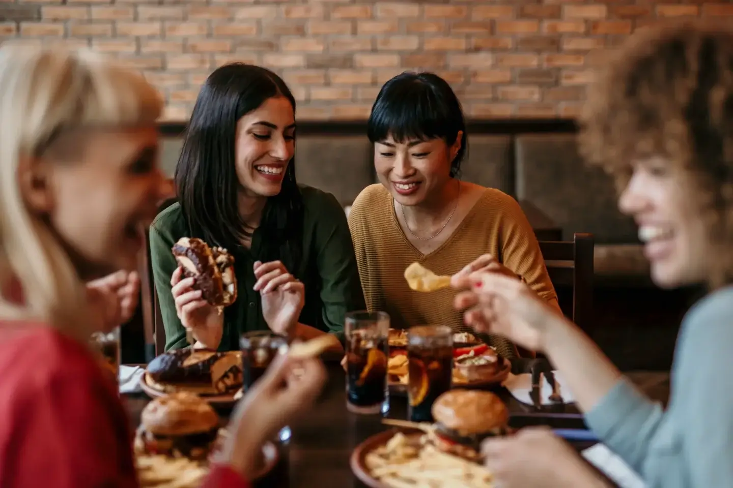 Group of friends gathering around a wooden table and passing plates of food while sharing a relaxed sit-down meal.
