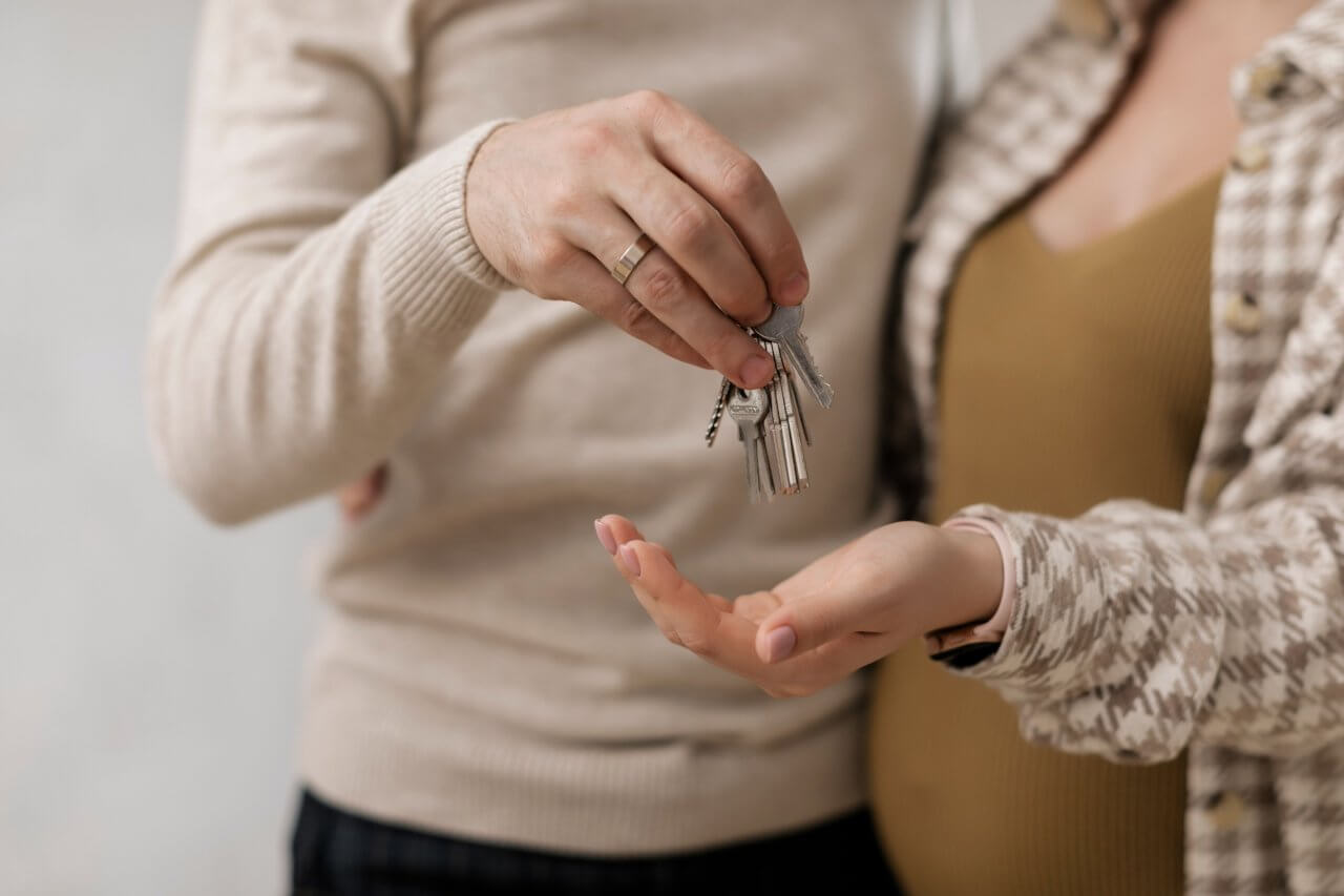 3 pexels-a-darmel-7641906 A close-up shot of a man handing a set of house keys into a woman's open hand while standing together indoors.
