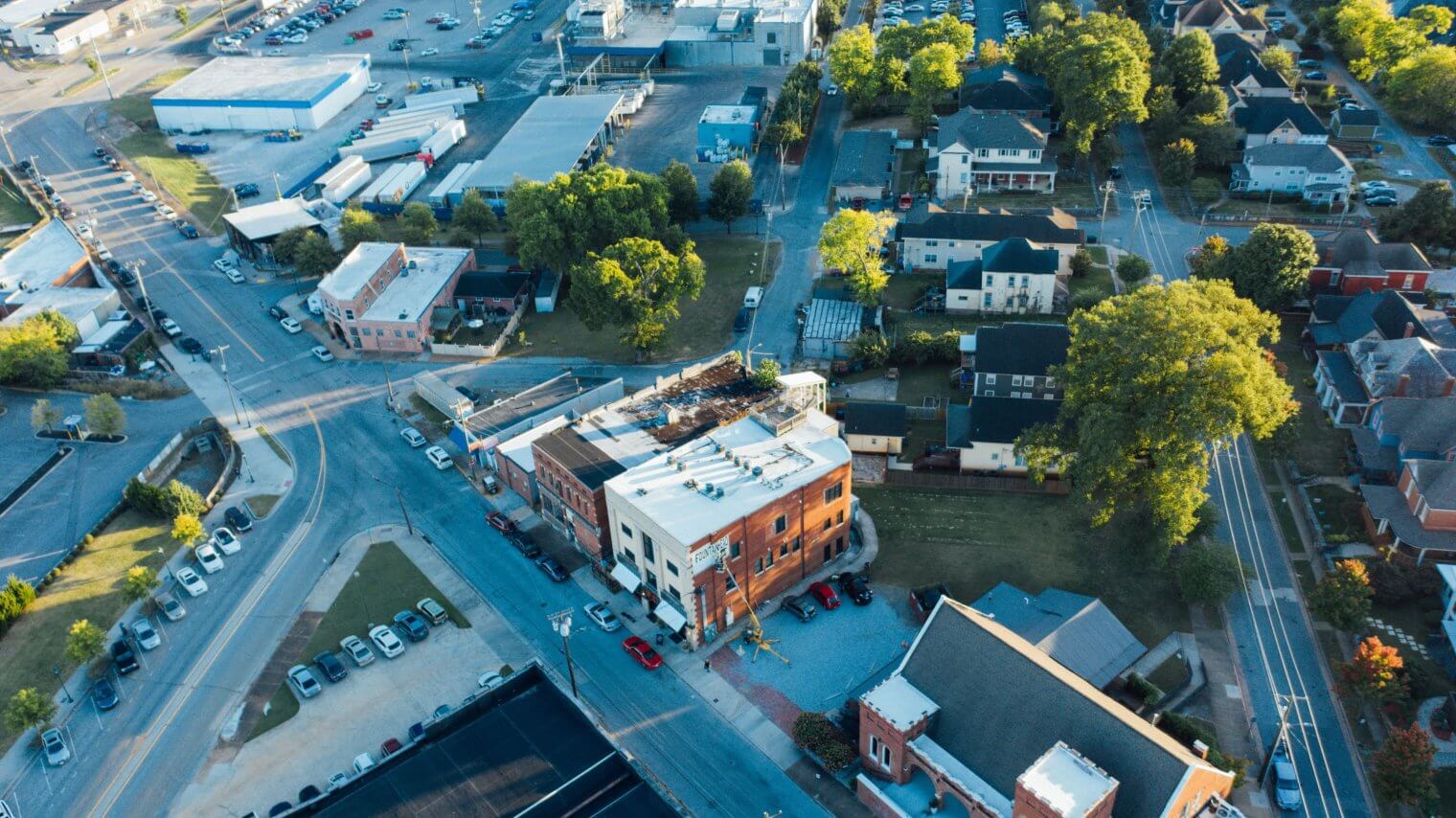 An aerial view showing a suburban neighborhood featuring streets, brick buildings, green trees, and parking lots.
